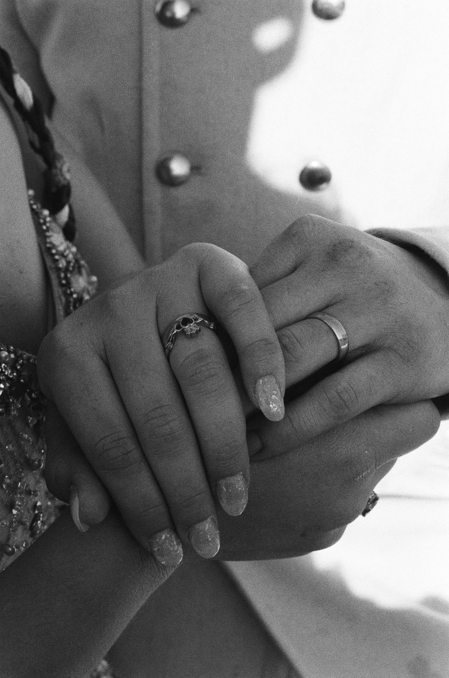 Black and white photo of newlyweds holding hands, showing wedding rings on their fingers, bride in lace dress.