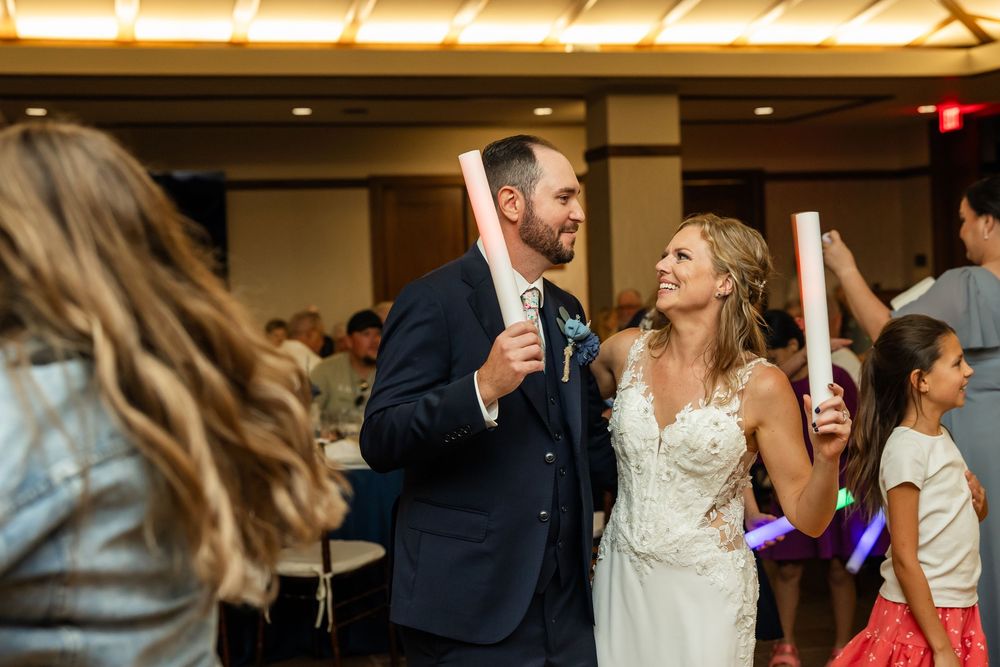 Bride and groom smile while holding glow sticks at their wedding reception celebration.