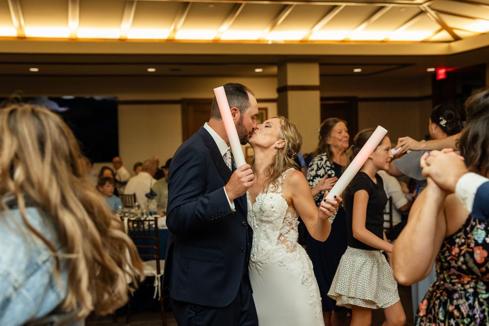 Bride and groom share a kiss on the dance floor surrounded by guests holding glow sticks at their wedding reception.