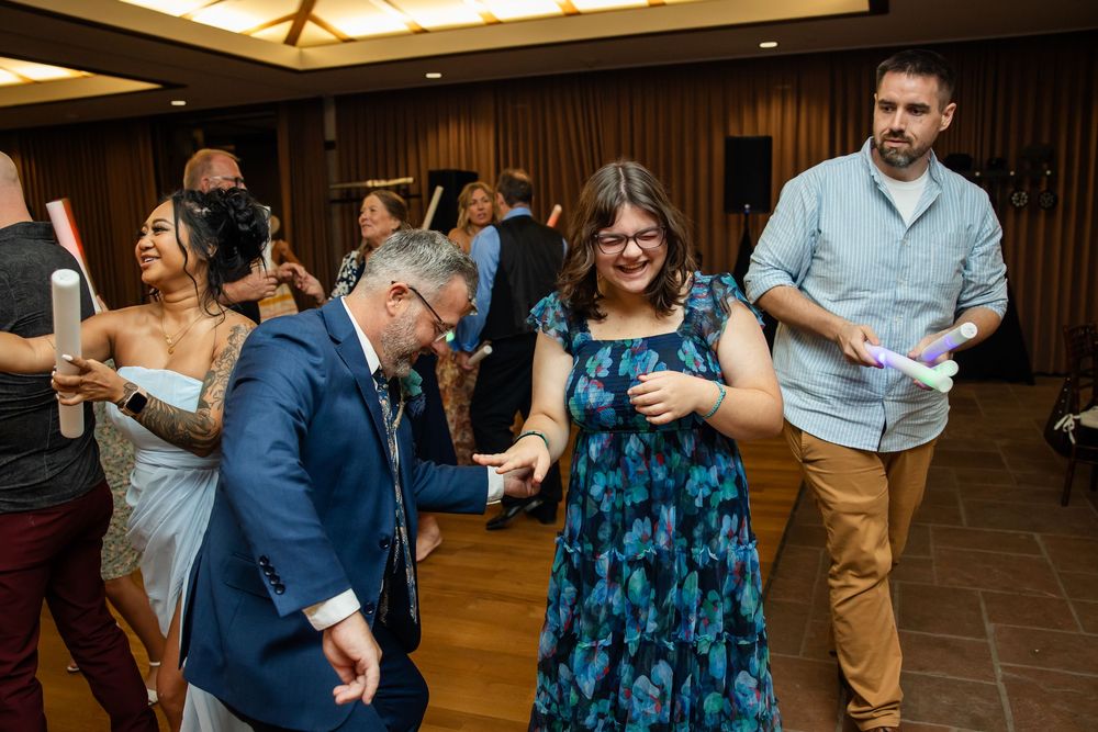 Guests dancing joyfully at a wedding reception, wearing formal attire and holding glow sticks on the dance floor.