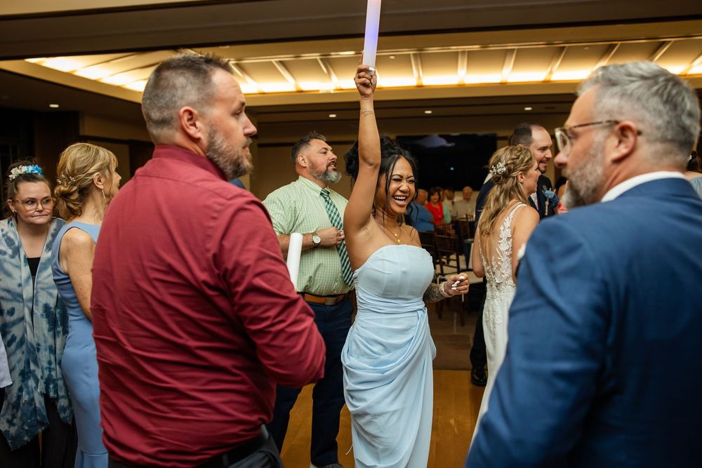 Guests dancing joyfully at a wedding reception, with a woman in a blue dress raising a glow stick.