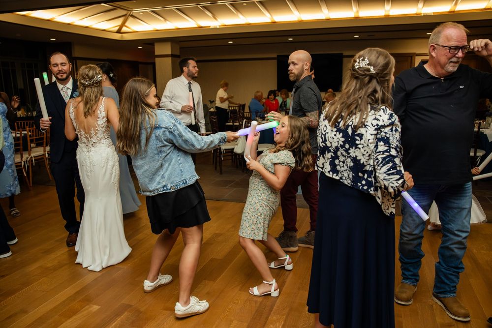 Guests dancing joyfully at a wedding reception on a wooden dance floor with glowing light sticks.