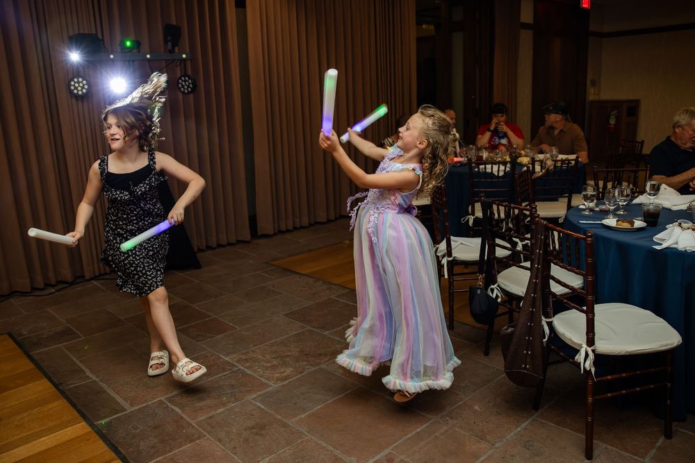 Two girls dance with glow sticks at an indoor party event with disco lights.