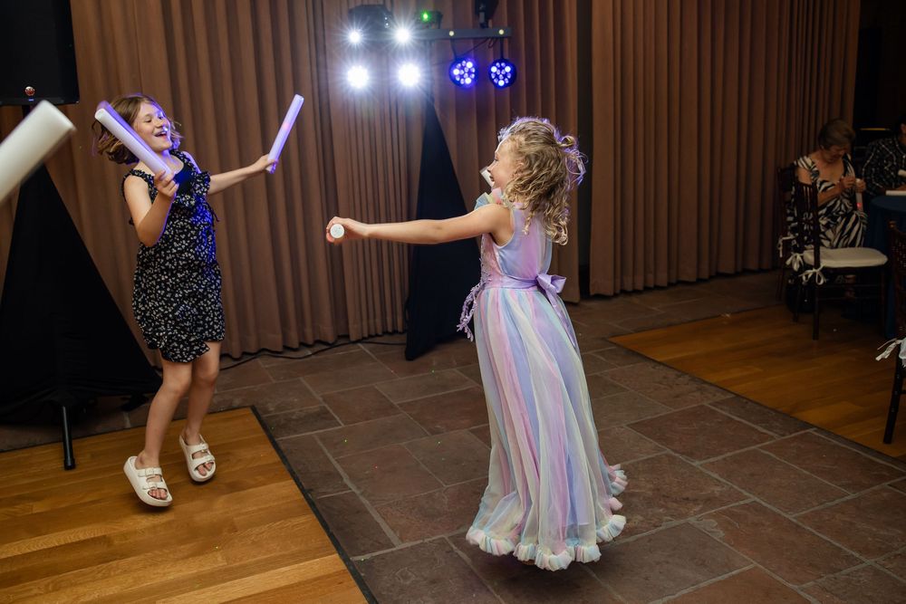 Two young girls play with glow sticks on a dance floor at a festive event.