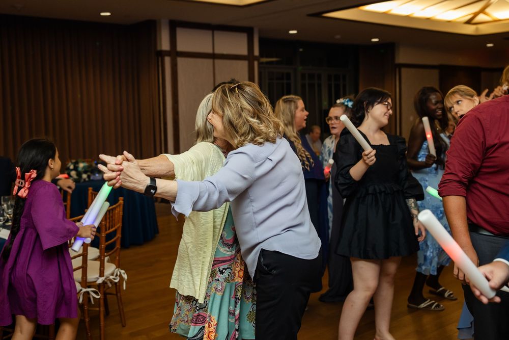 Guests dancing in a line at an indoor event or wedding reception in a decorated ballroom.