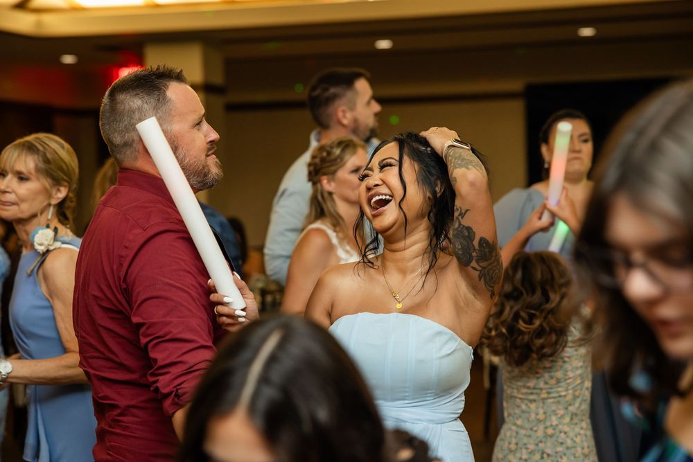 Joyful wedding reception guests dancing and laughing together in a ballroom, bride in white dress celebrating.