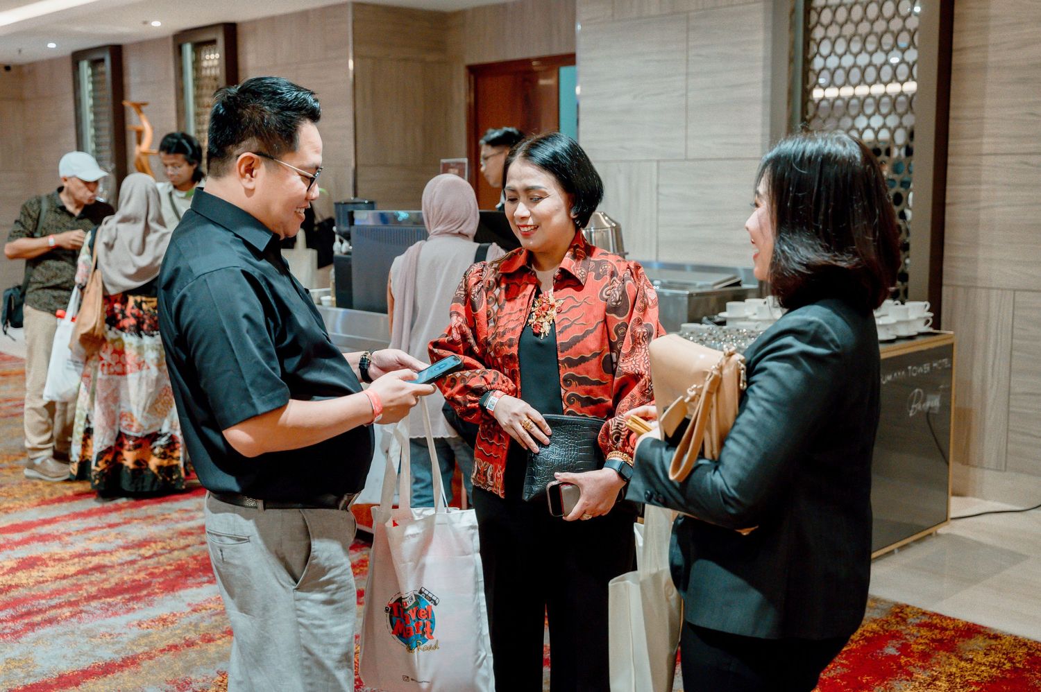Professionals in batik attire exchanging business cards at a formal networking event in an elegant venue.