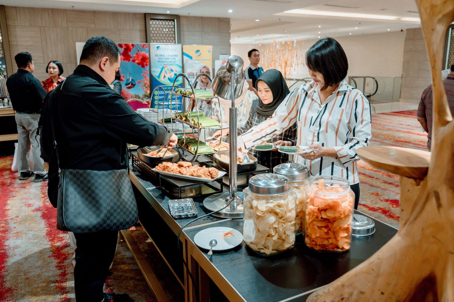 Guests serving themselves at an elegant hotel buffet spread with large glass jars of pickled foods on display.
