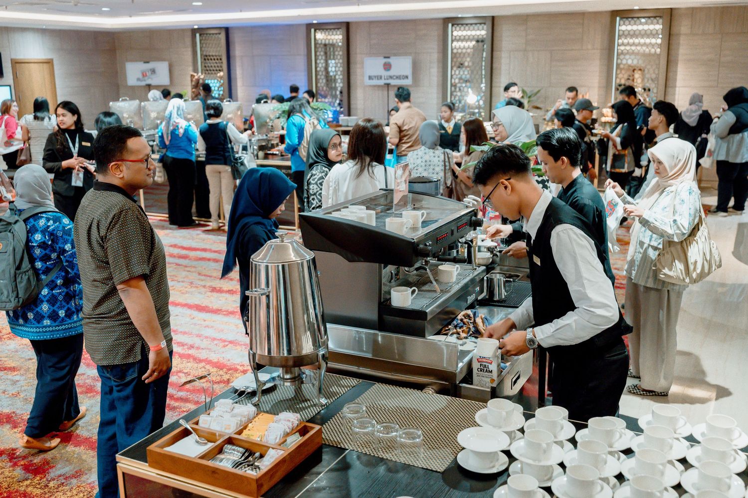 Barista preparing coffee at an espresso machine during a busy corporate event in a modern hotel ballroom.
