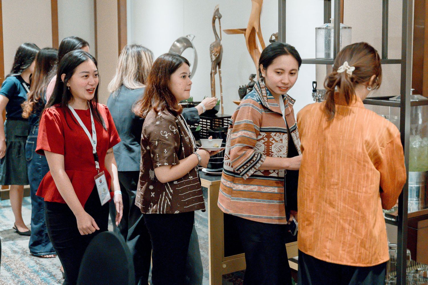 Women networking at an indoor cultural event, examining handcrafted artifacts and decor in a elegantly decorated exhibition space.