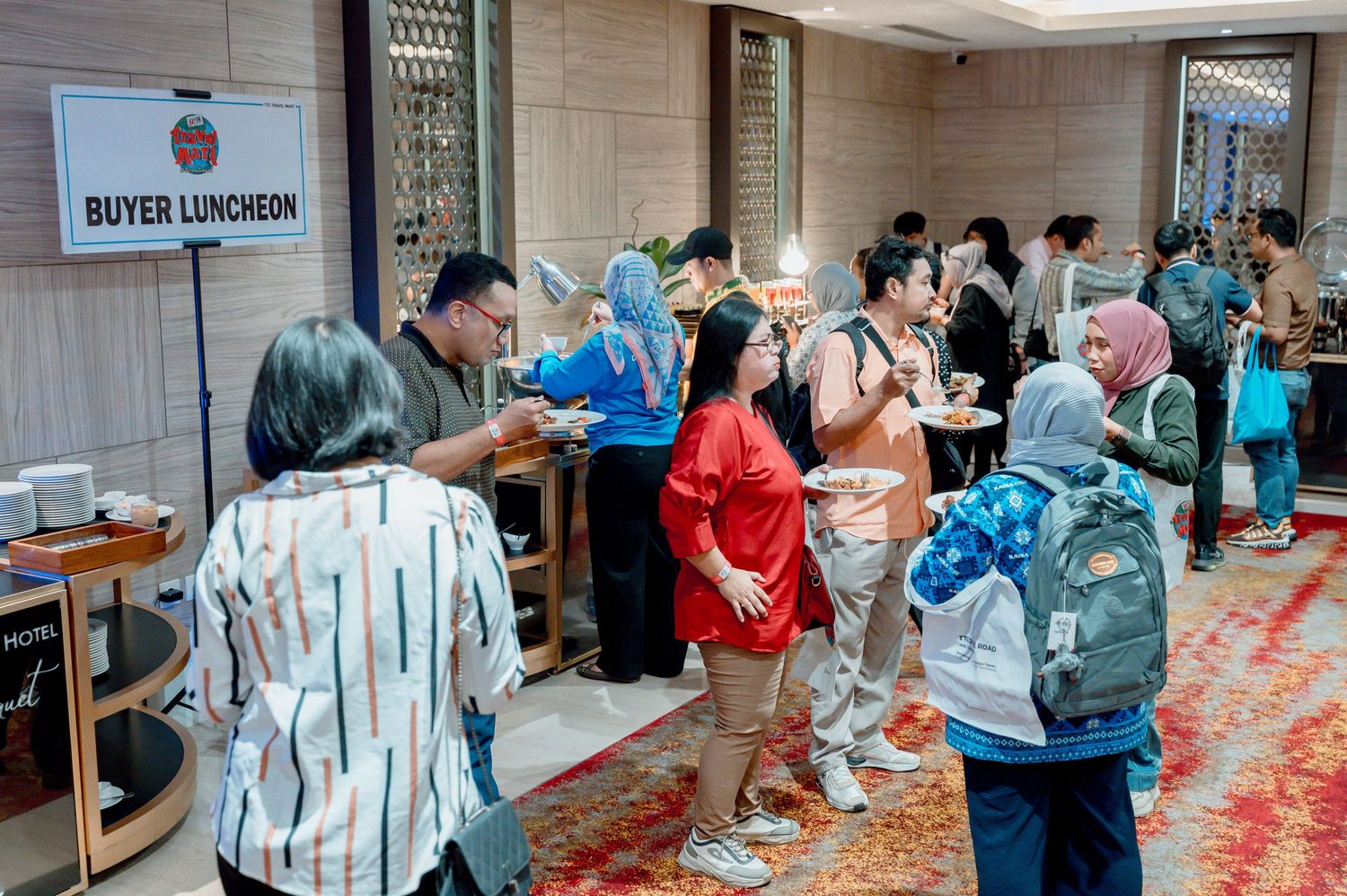 Guests line up at a Buyer Luncheon event in a hotel ballroom, with attendees wearing name badges and casual attire.