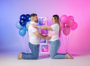 Excited couple at gender reveal party with blue and pink balloons in studio.