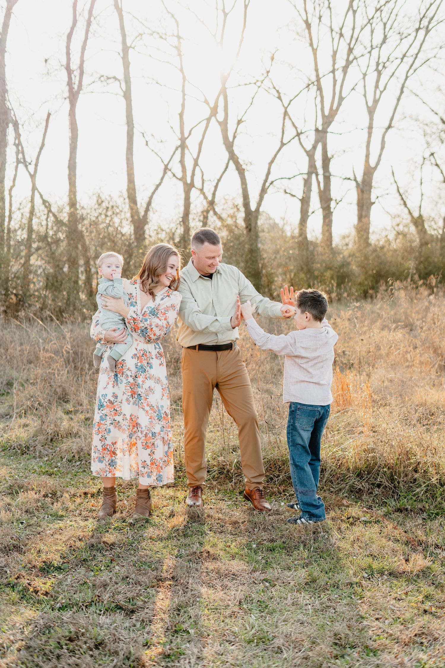 Family of four enjoying a sunny outdoor photo session in a field with bare trees in warm autumn light.