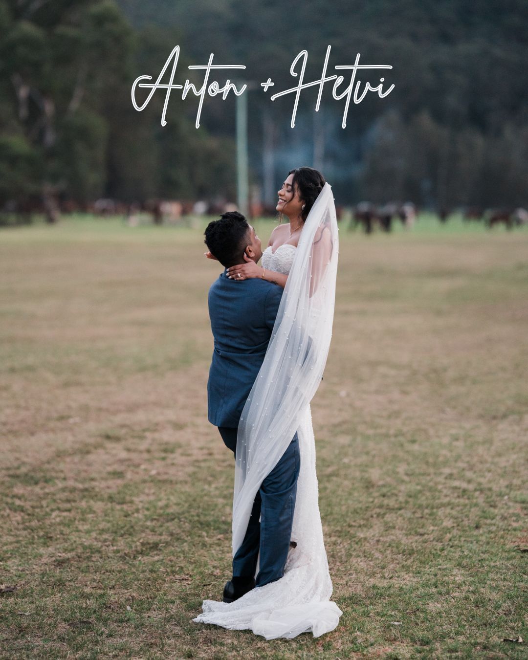Anton and Hetvi wedding couple embrace in a field, bride in white gown with veil, groom in blue suit.