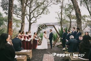 Wedding ceremony in forest clearing with bridal party in burgundy dresses at hexagonal arch altar.