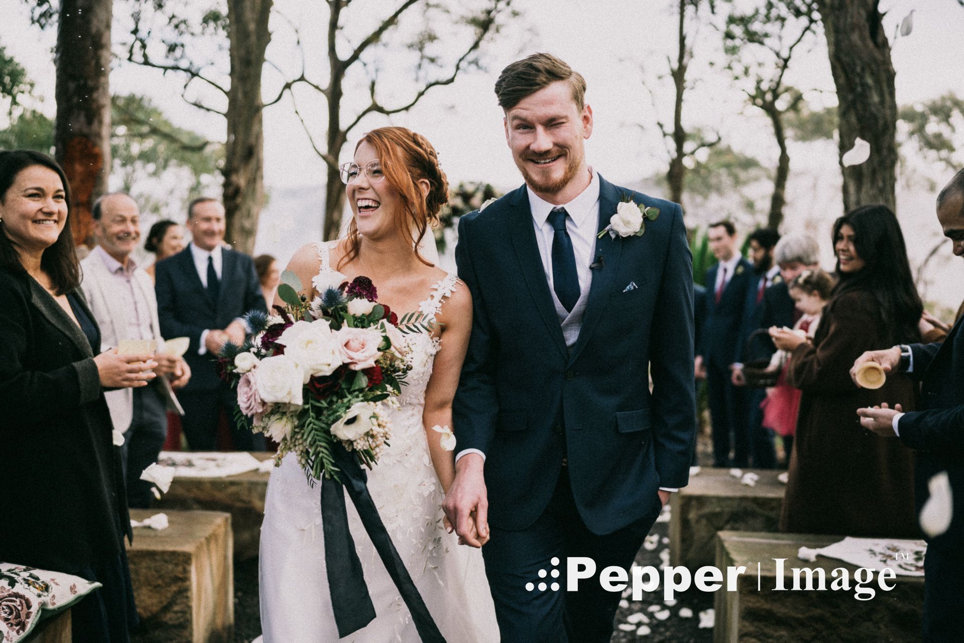 Newlyweds walk back down aisle smiling as guests celebrate with confetti at outdoor wedding ceremony.