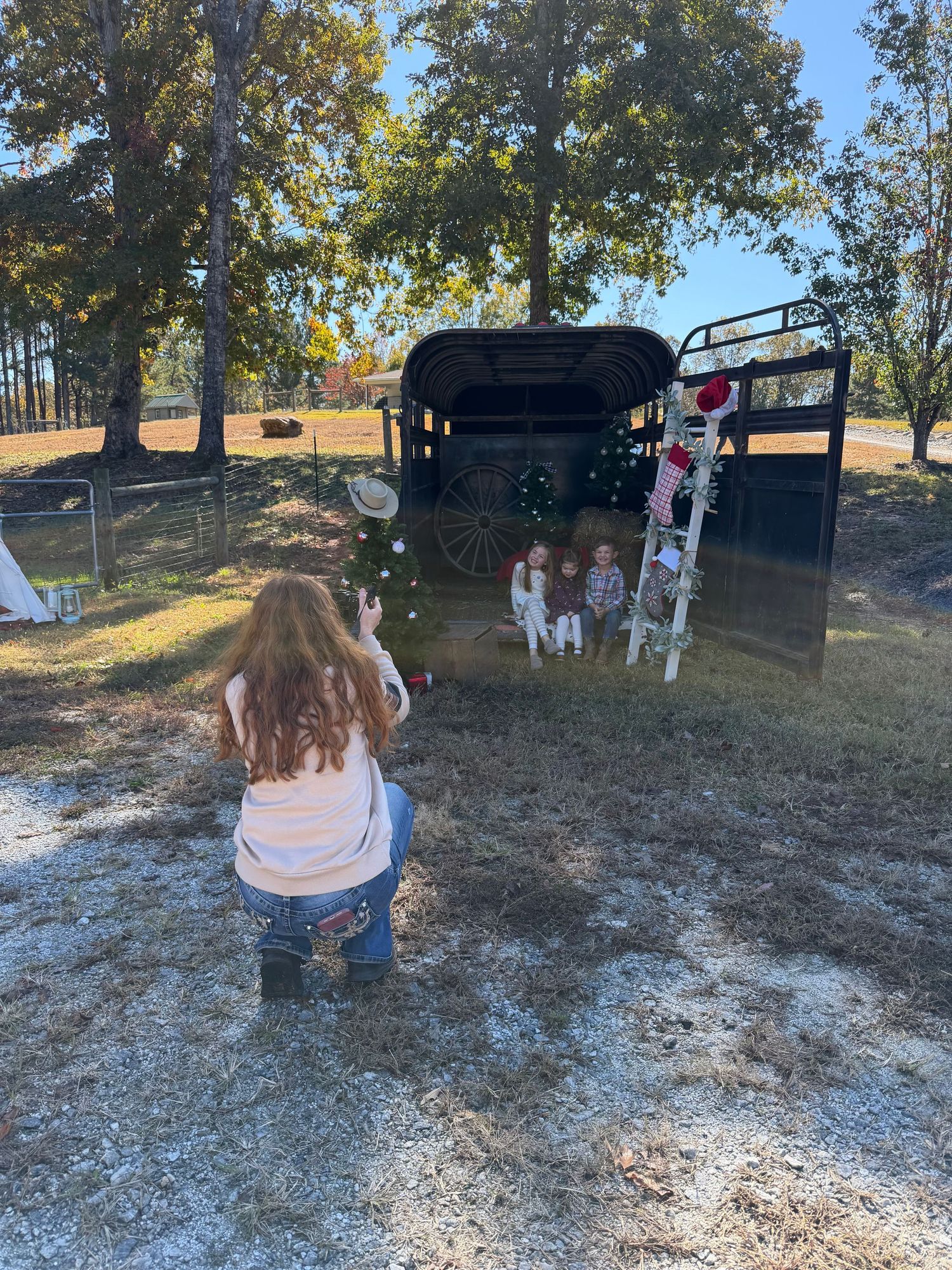 Woman photographing three young children posed in decorated horse trailer outdoors.
