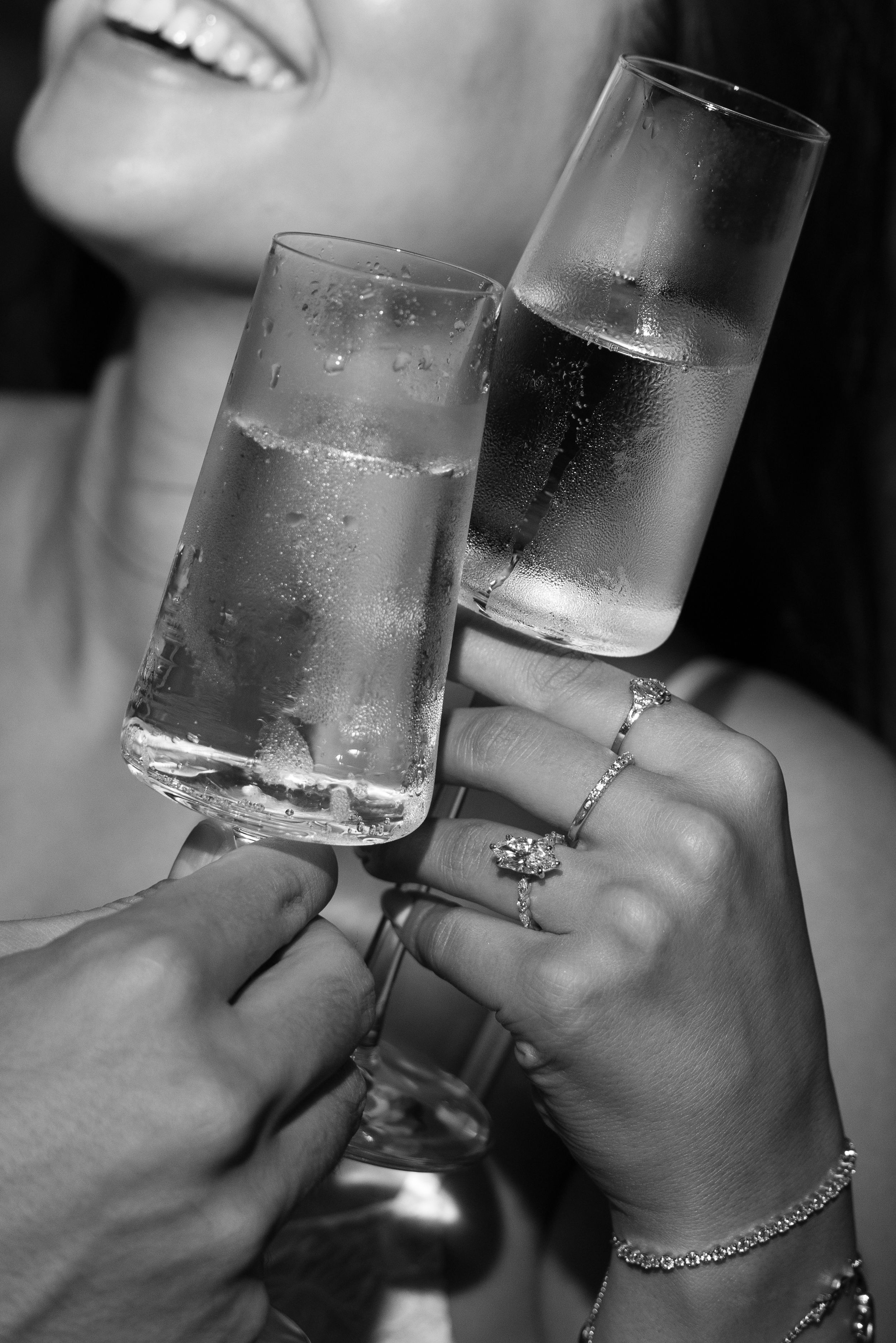 Black and white photo of couple toasting with champagne flutes, woman wearing diamond ring and bracelet.