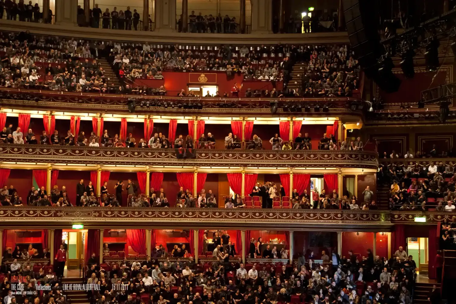 Packed audience fills ornate red-lit balconies at Royal Albert Hall during a grand performance.