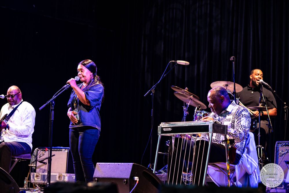 Live band performance on stage with vocalist and musicians playing guitar and drums under bright lights.