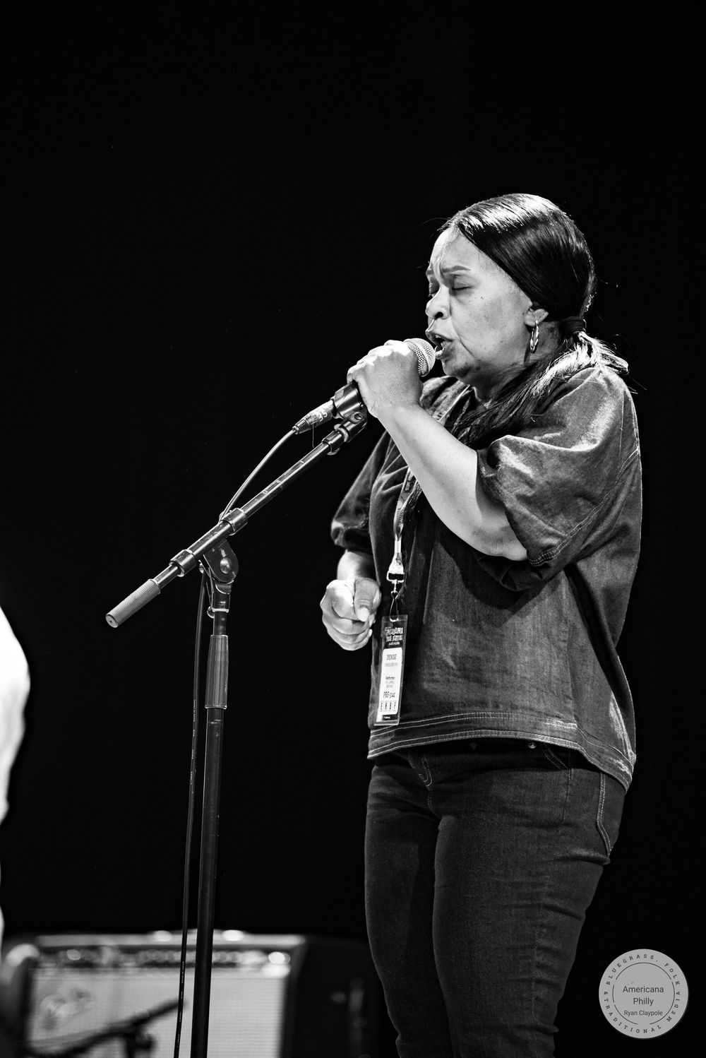 Black and white photo of a woman singing passionately into a microphone on stage during a live performance.