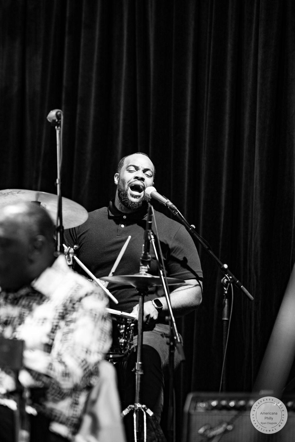 Male vocalist singing passionately into microphone on stage during live jazz performance.