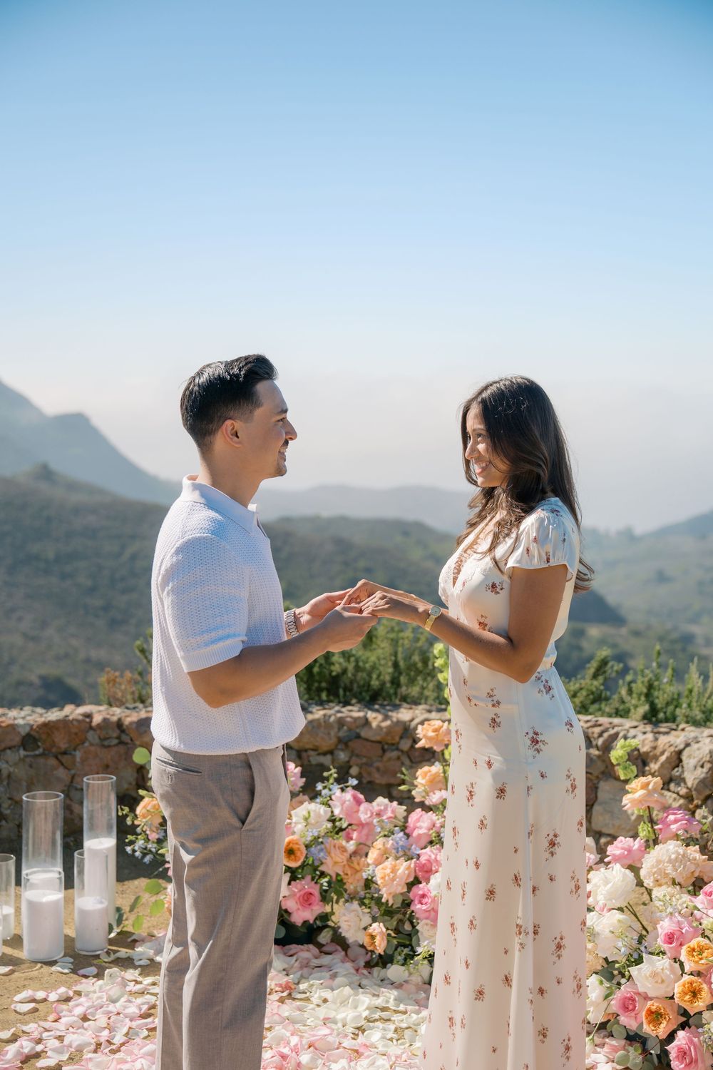 Man placing engagement ring on woman's finger at stunning outdoor proposal site with mountain views.