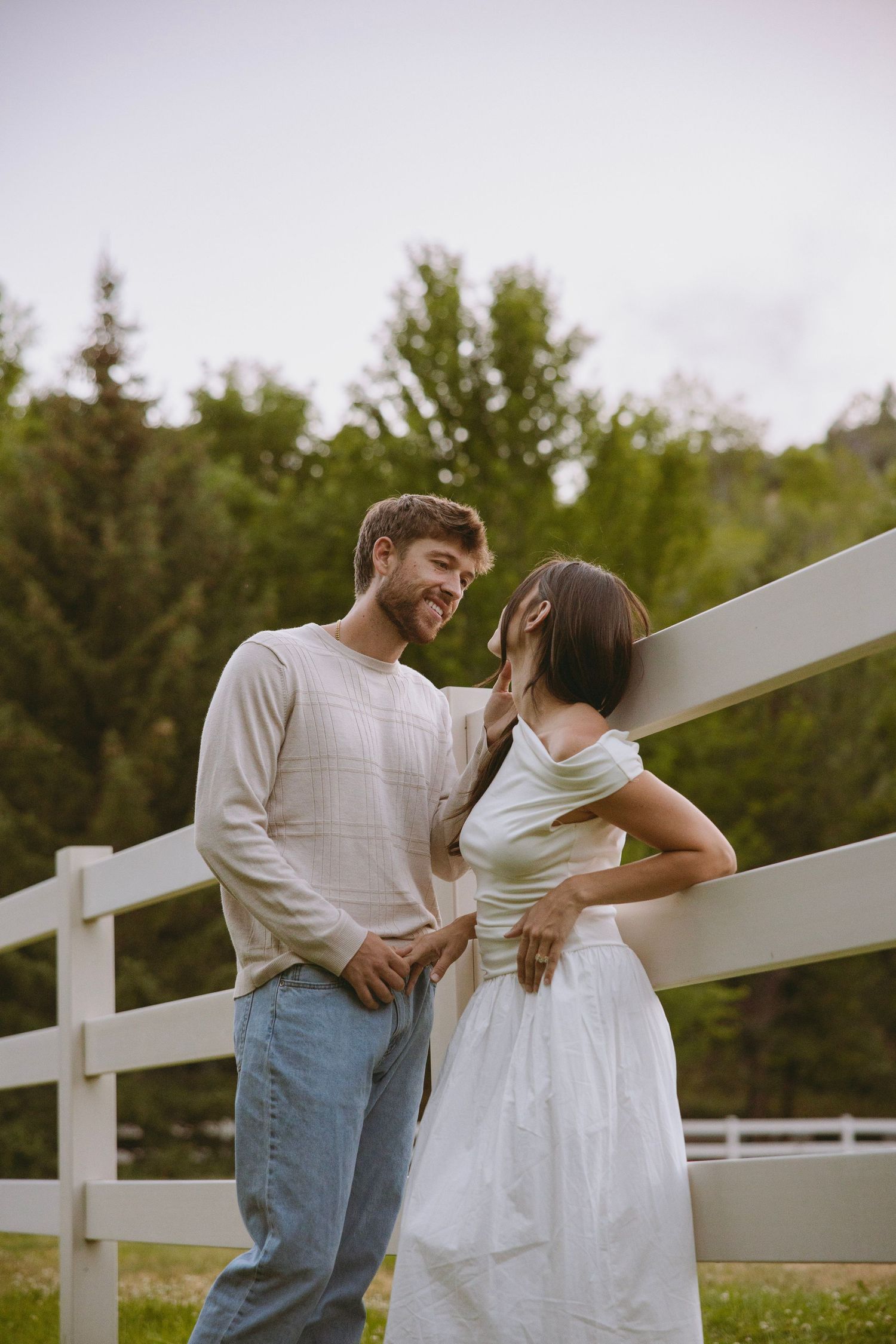 A couple shares an intimate moment along a forest path lined with evergreen trees and birch during a wedding photo session.