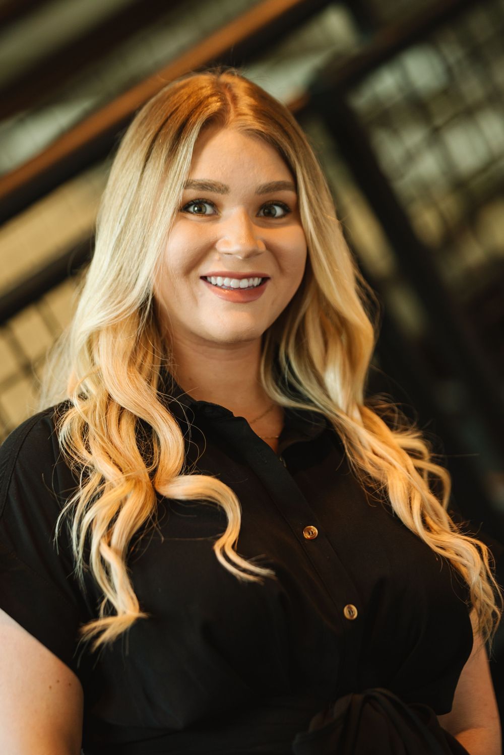 Smiling blonde woman in black dress shirt with wavy hair poses for a professional portrait photo.