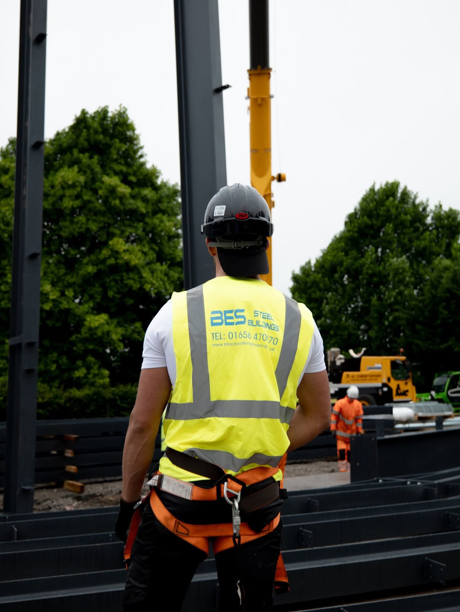 BES construction worker in hi-vis vest and hard hat overseeing steel frame building site with crane.