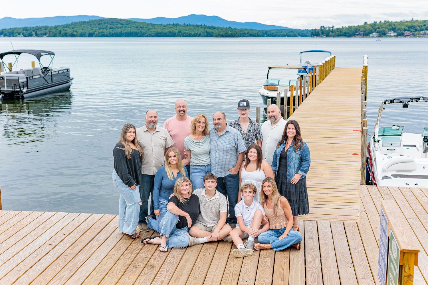 Large extended family poses together on wooden dock beside lake with mountains in background. Weirs Beach Laconia NH