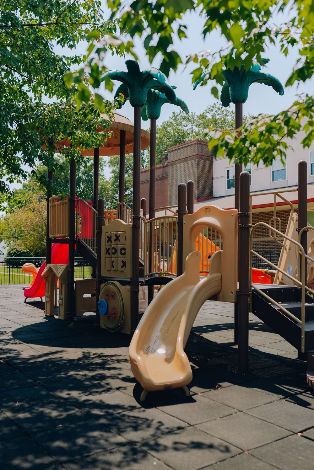 Colorful children's playground with slides and palm tree decorations on rubber flooring near a building.
