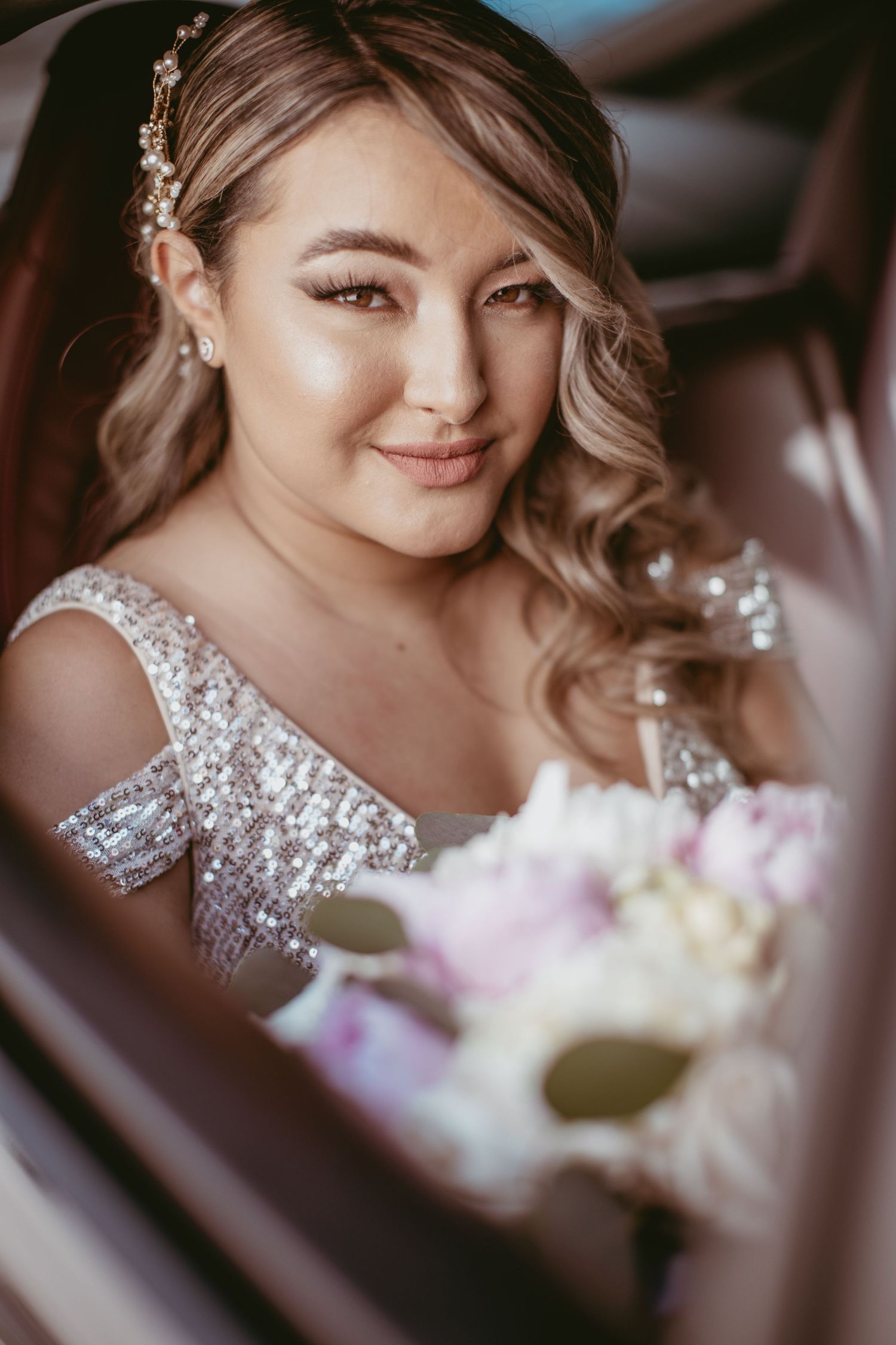 Close up portrait of bride wearing sparkly dress and floral headpiece while holding bouquet.