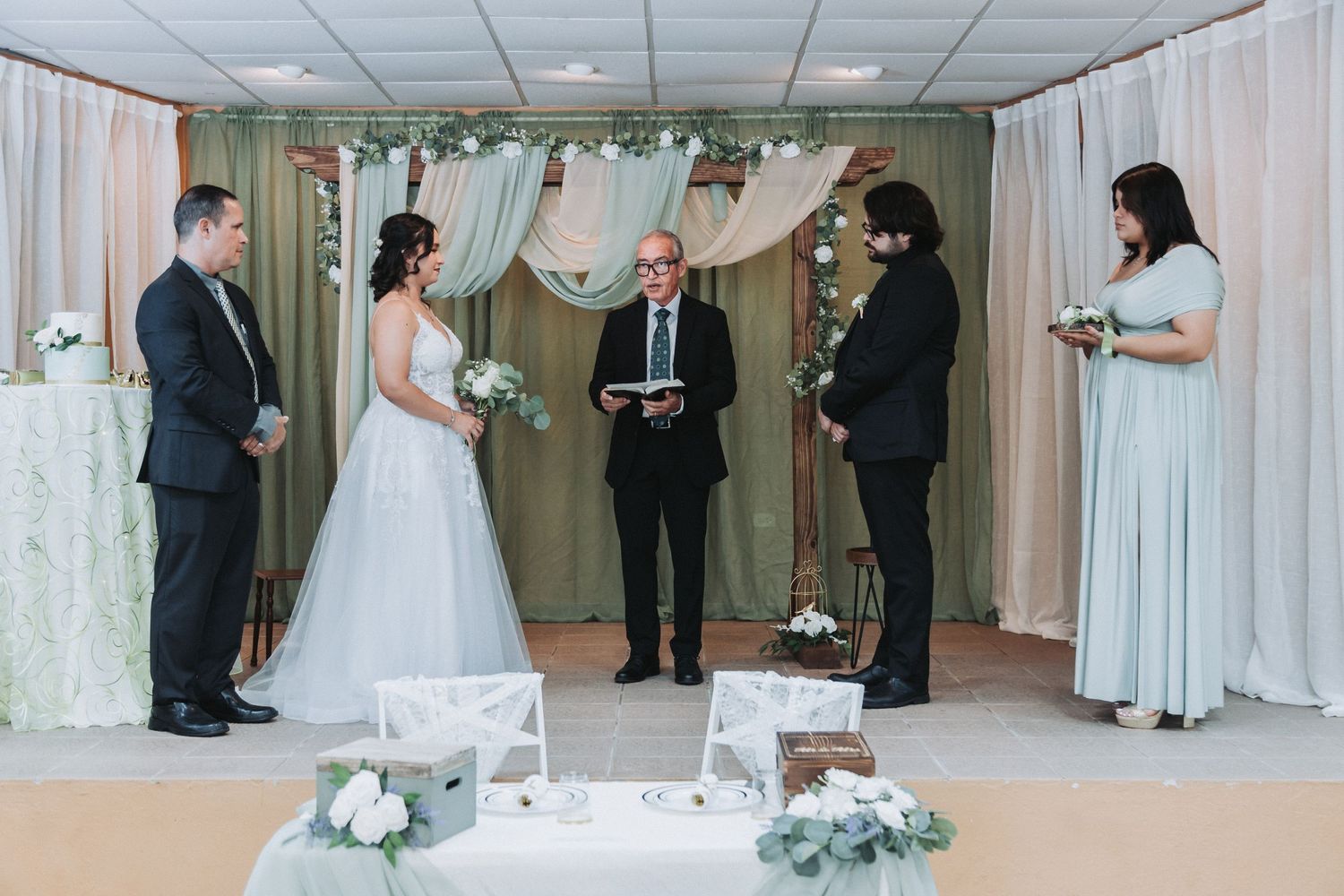 A wedding ceremony in progress with white fabric draping and floral decorations.