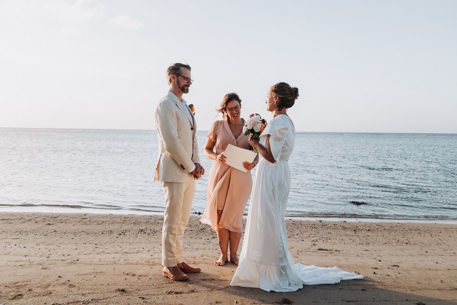 Intimate beach wedding ceremony with small group gathered by the ocean at sunset.