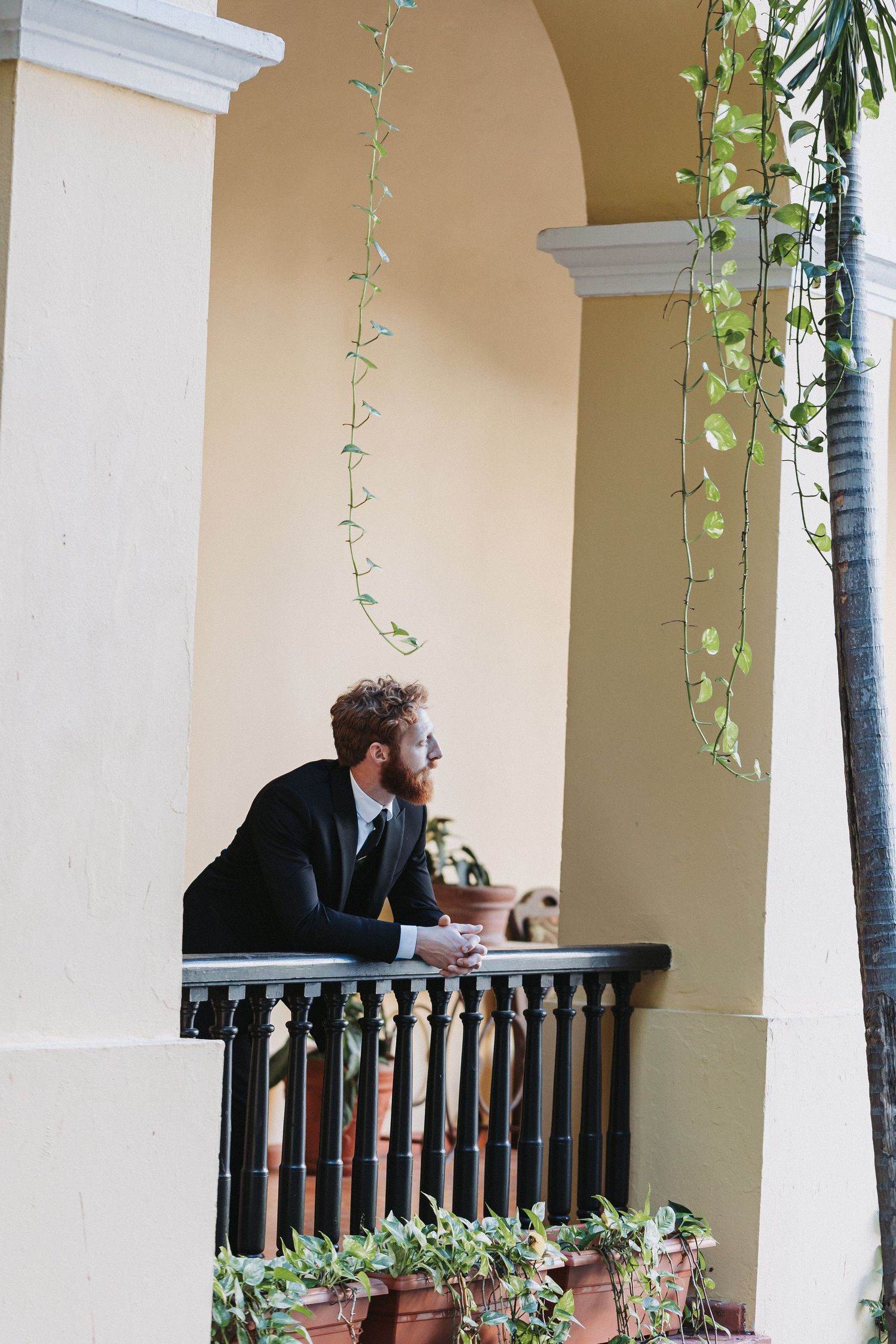 Side view of someone in formal attire sitting on a balcony with hanging vines.