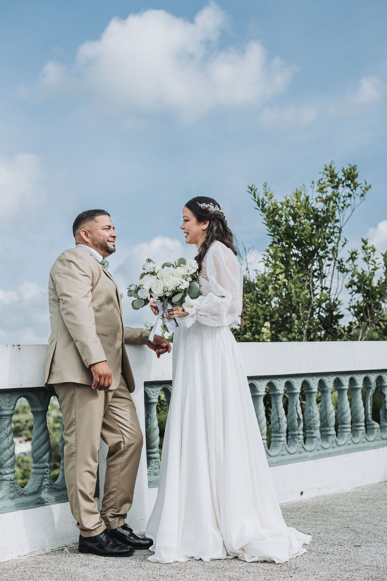 Outdoor wedding portrait with stone balustrade and blue sky background.