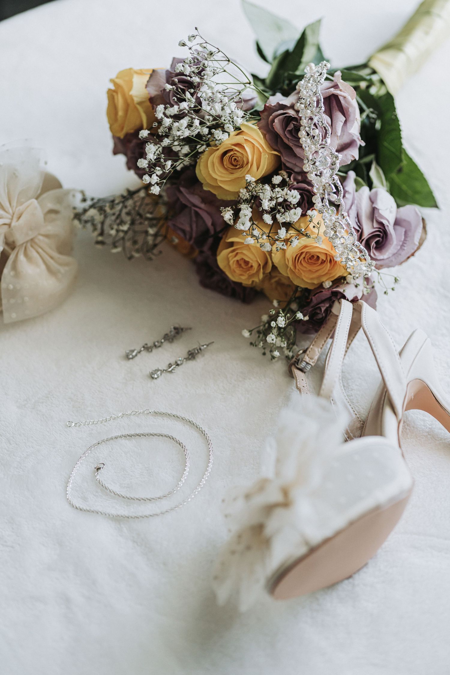 Wedding bouquet with peach roses and baby's breath lying next to bridal shoes.