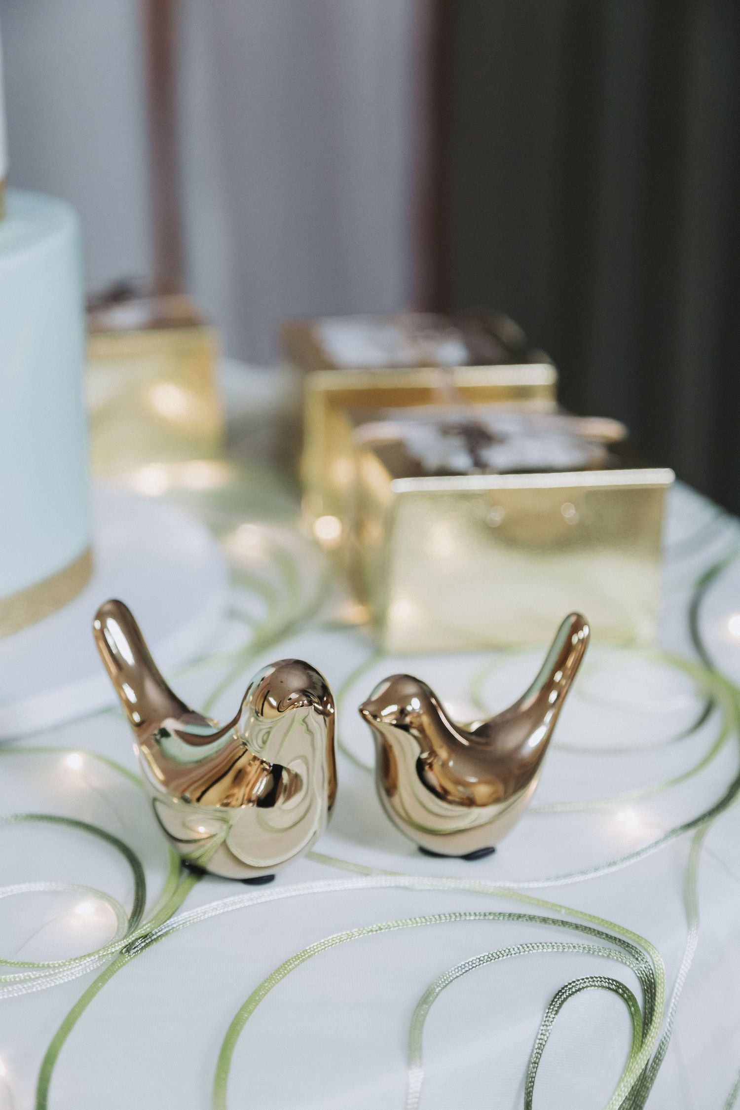 Two decorative golden bird figurines displayed on a white tablecloth with string lights.