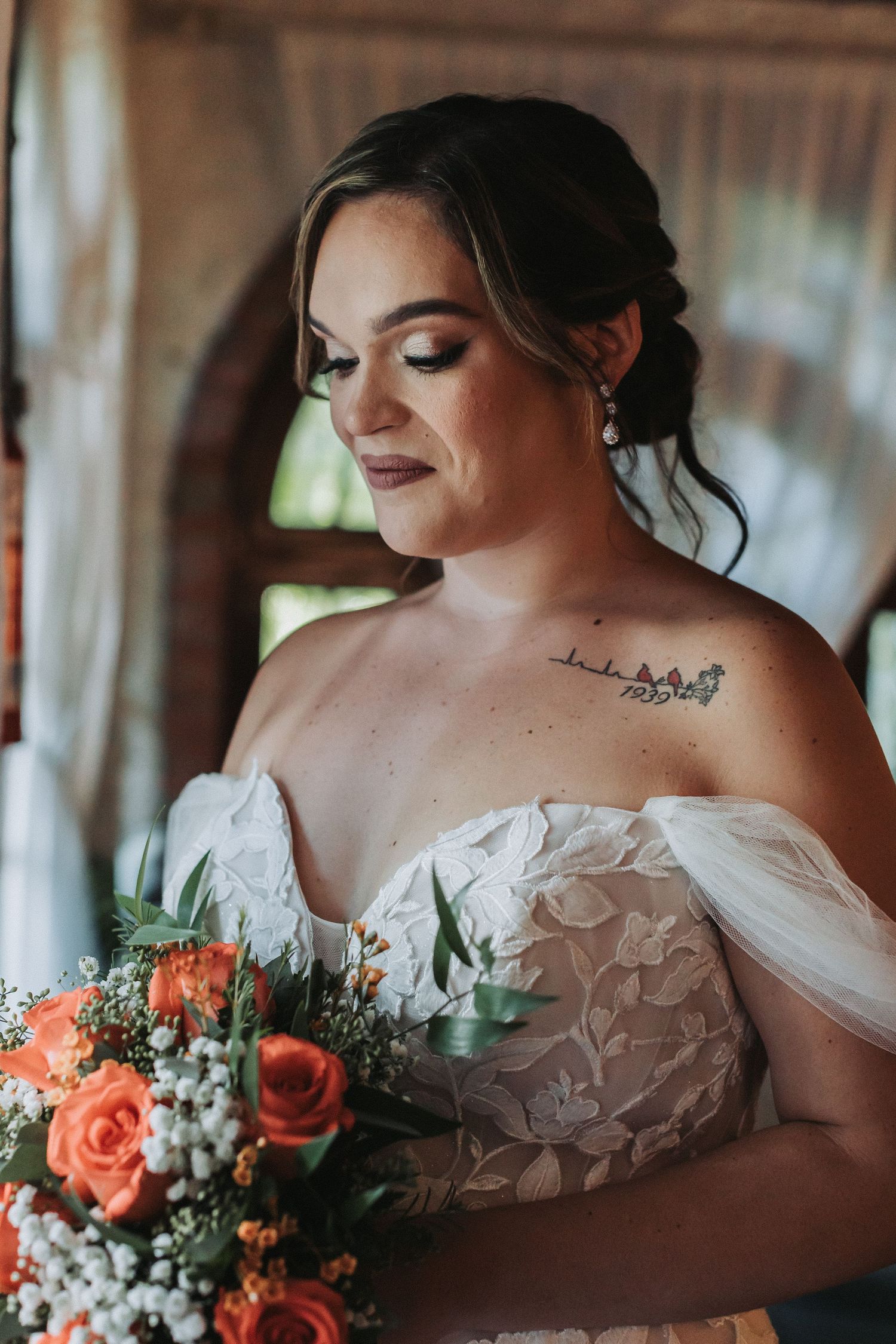 A portrait of a bride holding a coral rose bouquet in a detailed lace wedding gown.