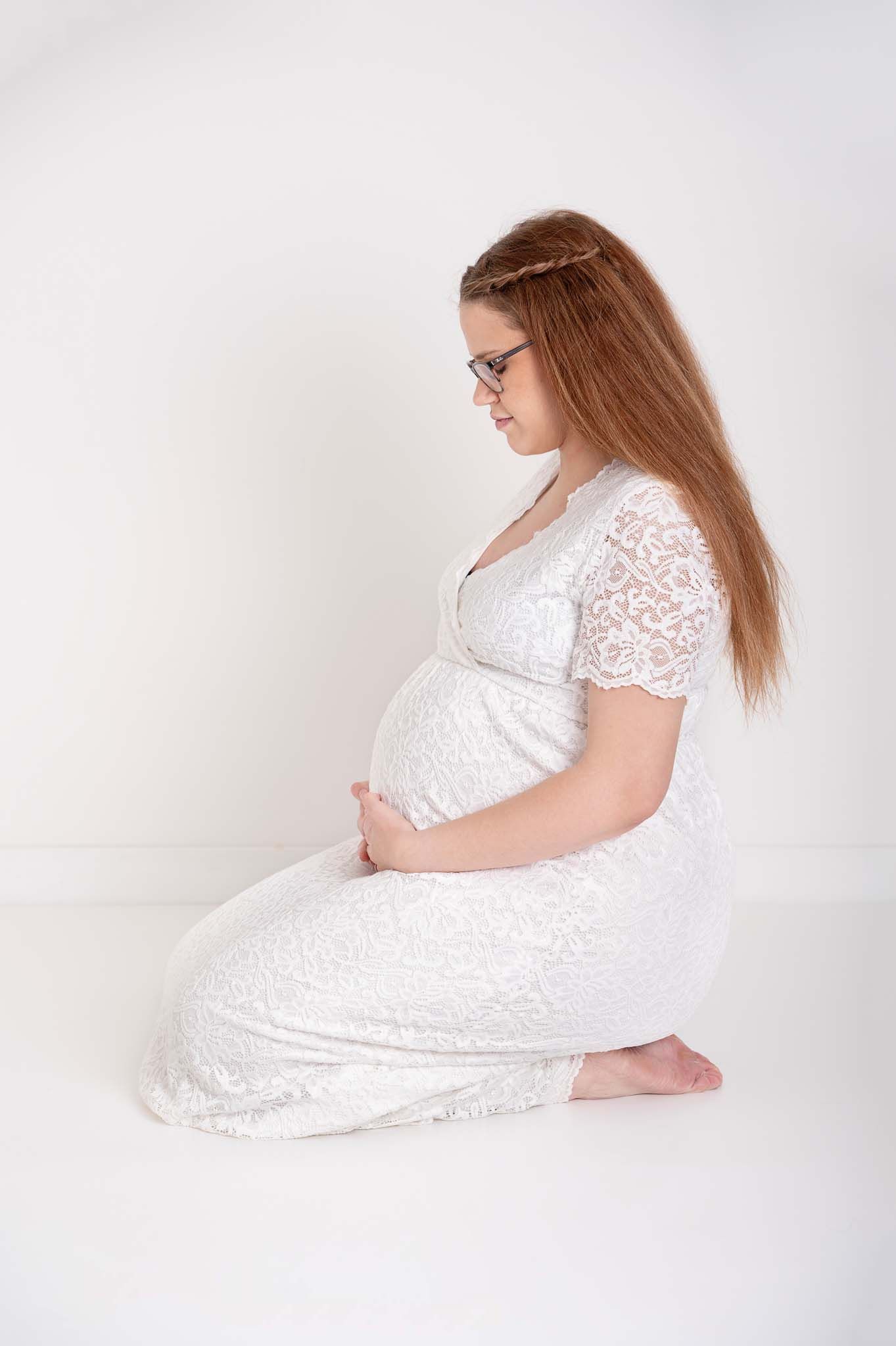 Expecting mom sits on knees with head down, eyes closed deep in thought in studio maternity session in Baltimore Ontario.