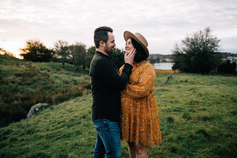 A couple shares a romantic moment in a lush green field at sunset, woman in yellow dress and hat.