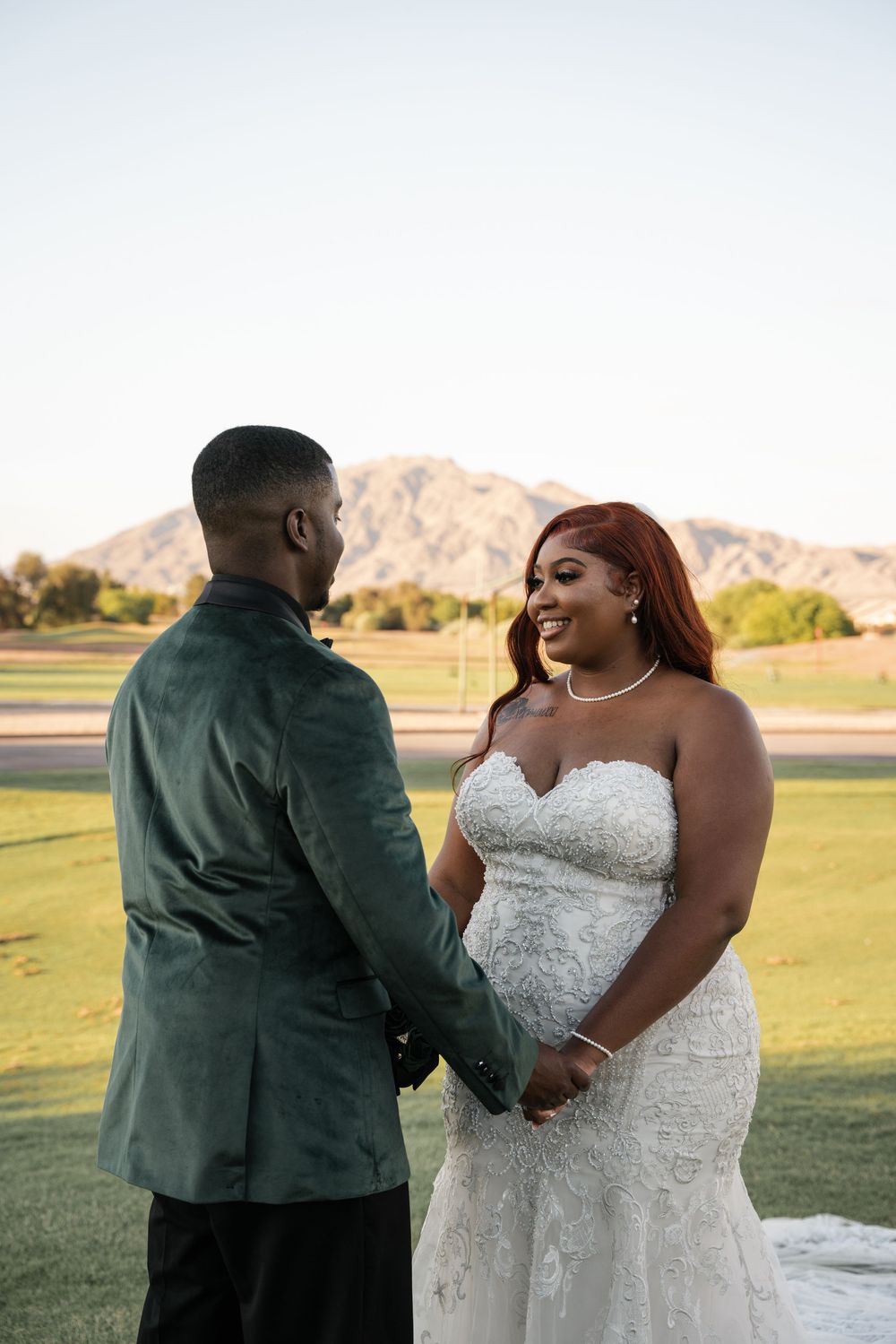 A bride and groom hold hands on a golf course at sunset, with mountains in the background, sharing a joyful wedding moment.