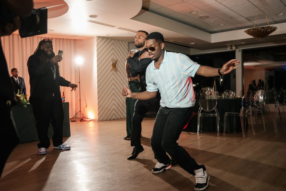 People dancing energetically at an indoor event venue with warm lighting and elegant decor.