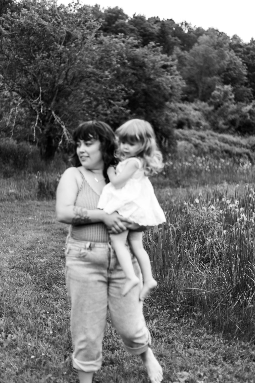 Black and white photo of a woman holding a young child in a meadow with trees in the background.