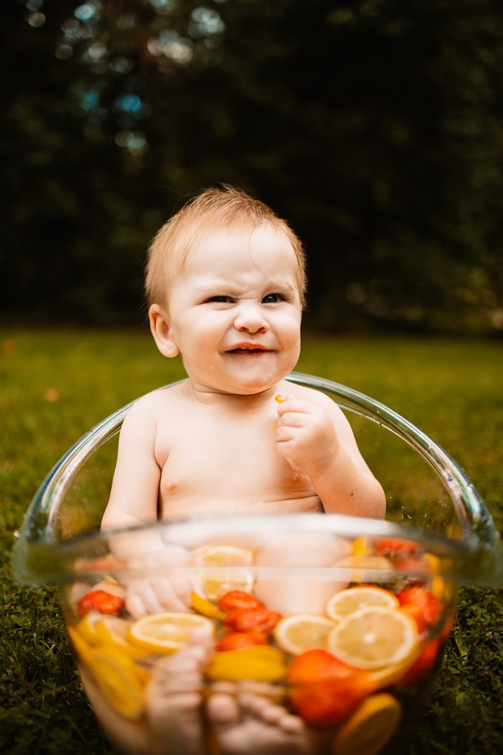 Smiling baby sitting in a fruit-filled glass bowl with lemons and strawberries on green grass in Oak Ridge, TN.