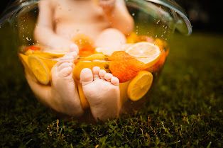 Baby feet peek out from a glass bowl filled with fresh orange and lemon slices on green grass in Oak Ridge, TN.