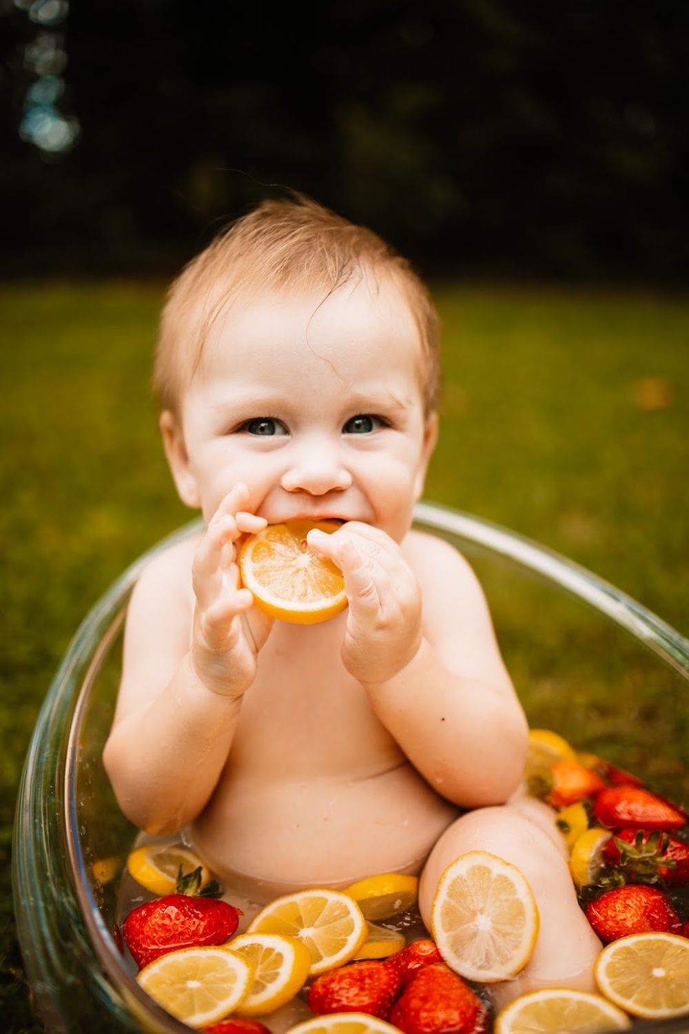 Happy baby biting a lemon slice while sitting in a glass bowl with strawberries and citrus fruits in Oak Ridge, TN.
