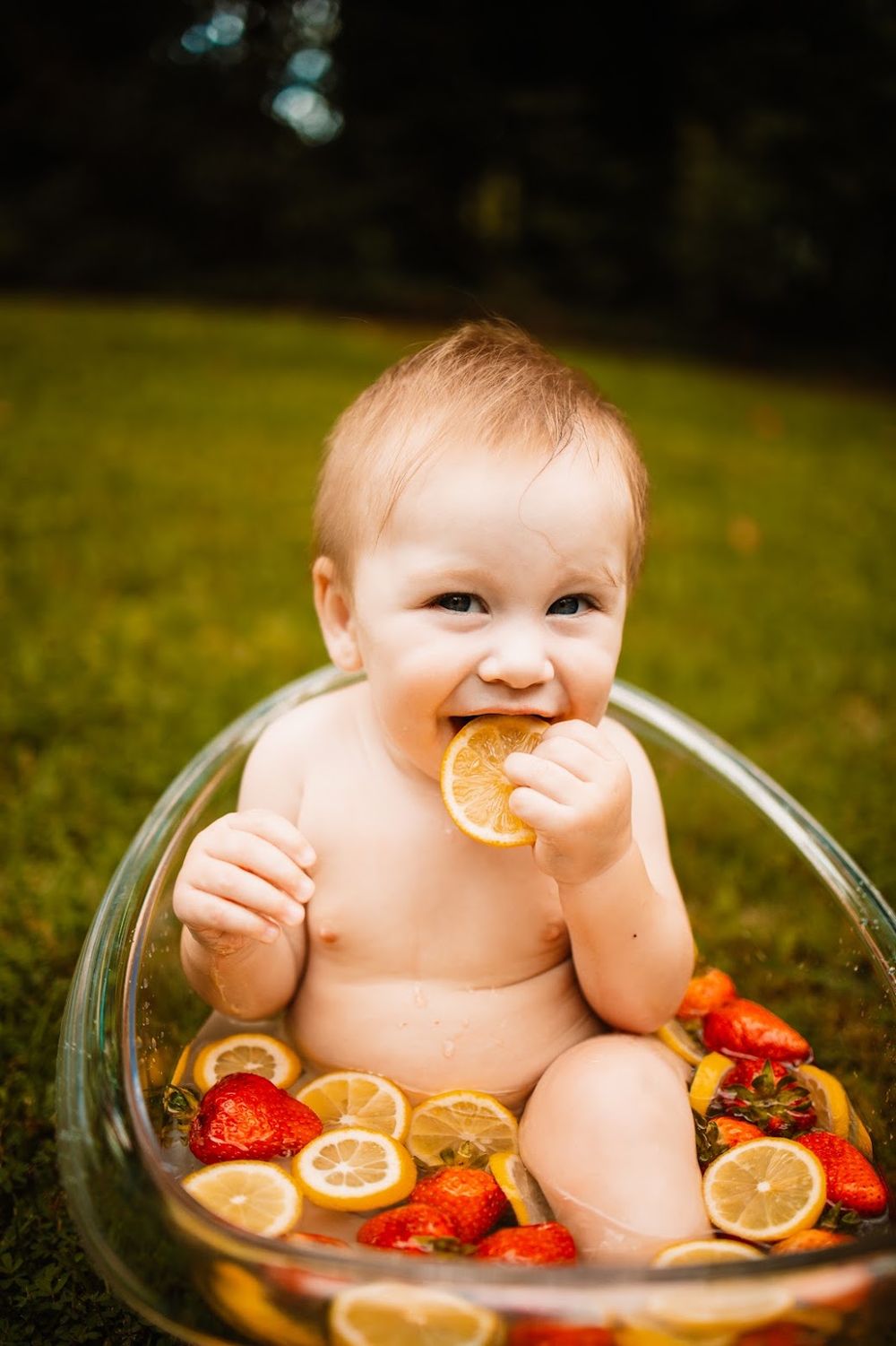 Baby sitting in glass tub with lemon slices and strawberries outdoors, chewing on a lemon slice in Oak Ridge, TN.