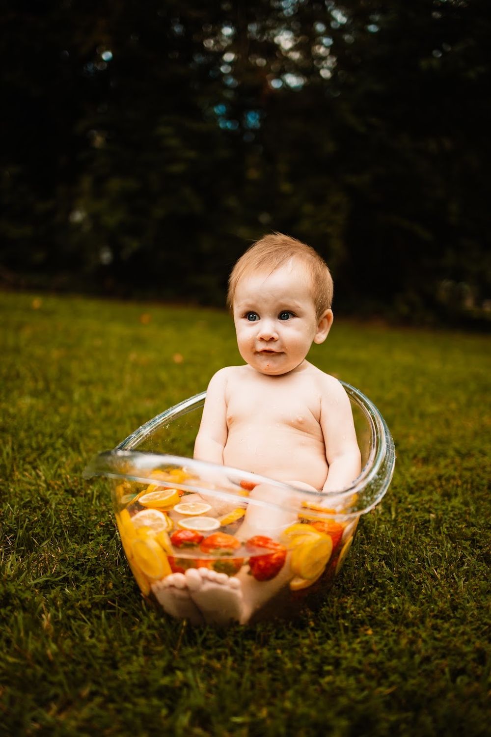 Curious baby sitting in clear tub with colorful citrus fruit slices outdoors on grass  in Oak Ridge, TN.